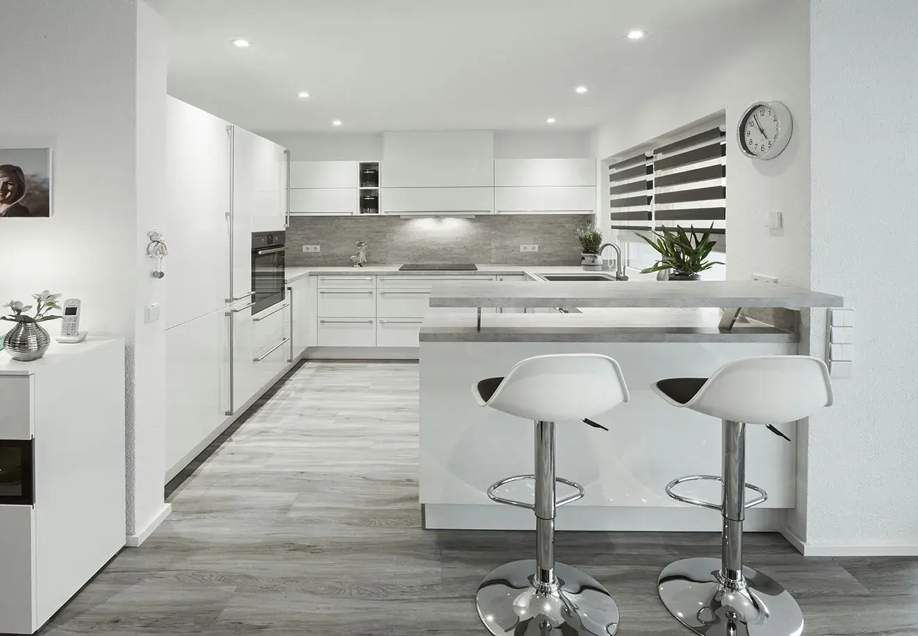Moderne weiße Küche mit Kochinsel, zwei Barhockern und grauem Boden.